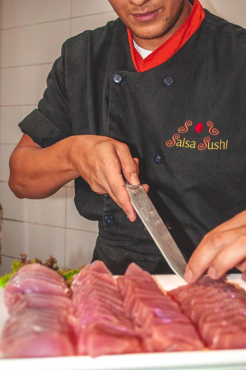 Sushiman do Salsa Self-Service, de dólmã Salsa Sushi, fatiando lombos de atum fresco